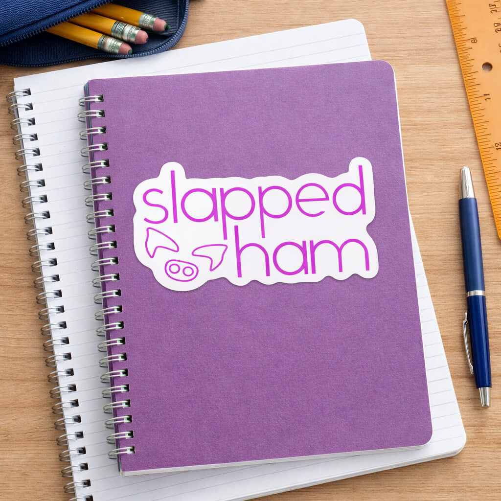 Purple notebook with 'slapped ham' sticker on a wooden surface with stationery items.