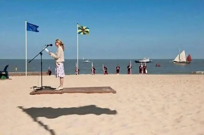 A woman giving a speech at the beach that looks like the podium is hovering.