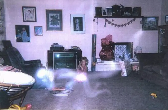 A mysterious photo of a young girl playing on the floor with a ghost in the foreground.