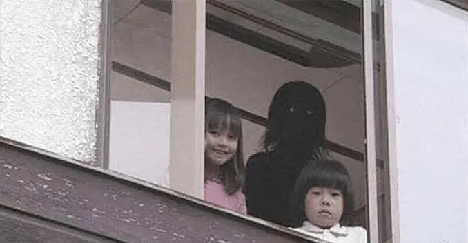 Two children stare out of a window with a scary shadow person behind them.