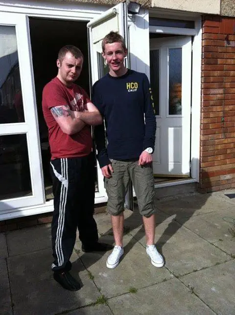 Two men pose for a photo, a possible ghost has appeared in the window.