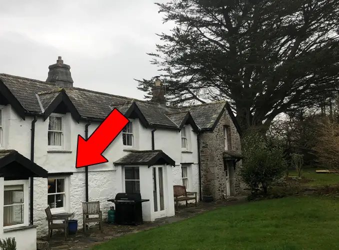 Photo of old house with mysterious cloaked figure in the window.